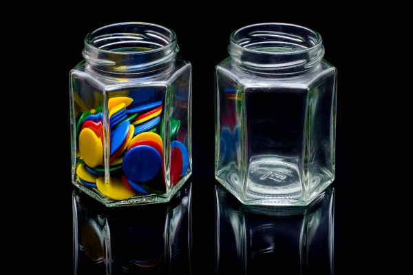 Two small jam jars, one full of plastic counters, one empty.