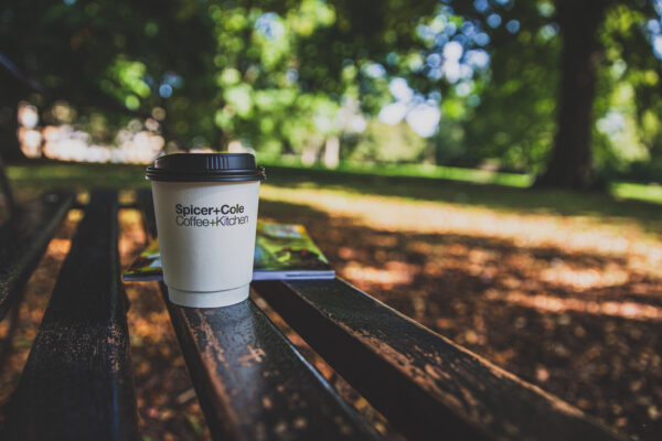 Spicer+Cole take-away coffee cup on a bench in the sunshine