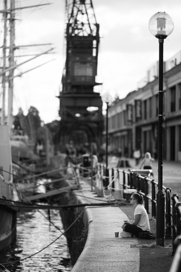 A woman sits serenely on the harbourside against the backdrop of the M Shed cranes
