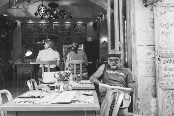 A man reads a newspaper at an outside café table in the Greek city of Rethymnon