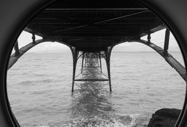 A view under Clevedon Pier with a stirring sea below, taken through a round window.