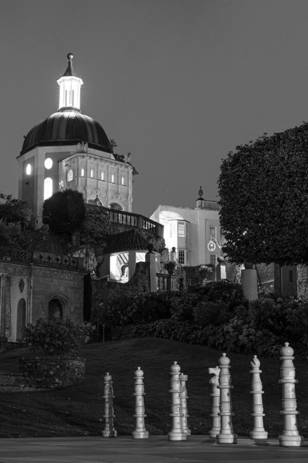 A night shot of the giant chess pieces on the chess board in the central square at Portmeirion, with the Green Dome in the background.